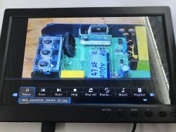 Small monitor with black bezel shows a close-up of a circuit board and an on-screen media player control bar.