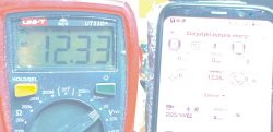 Multimetr pokazujący 12,33 V obok smartfona z aplikacją wskazującą 12,34 V