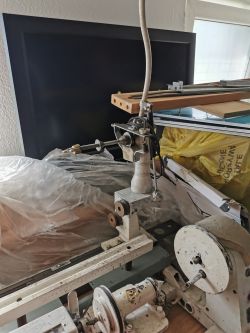 Fragment starej tokarki lub podobnej maszyny warsztatowej z metalowymi i drewnianymi elementami.