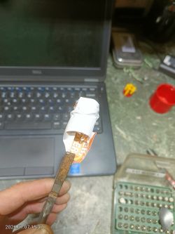 Zardzewiałe narzędzie z zaczepioną papierową naklejką, tło: laptop i stół warsztatowy