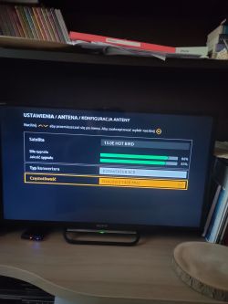 Ekran telewizora z menu konfiguracji anteny: satelita Hot Bird 13.0E i paski siły oraz jakości sygnału.