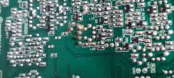 Zbliżenie na płytkę drukowaną (PCB) z widocznymi punktami lutowniczymi, ścieżkami i komponentami SMD; w jednym miejscu widoczne nadmiarowe lutowanie i pozostałości po topniku.