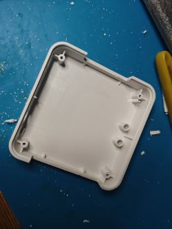 Empty plastic enclosure on a blue surface with a tool on the right.