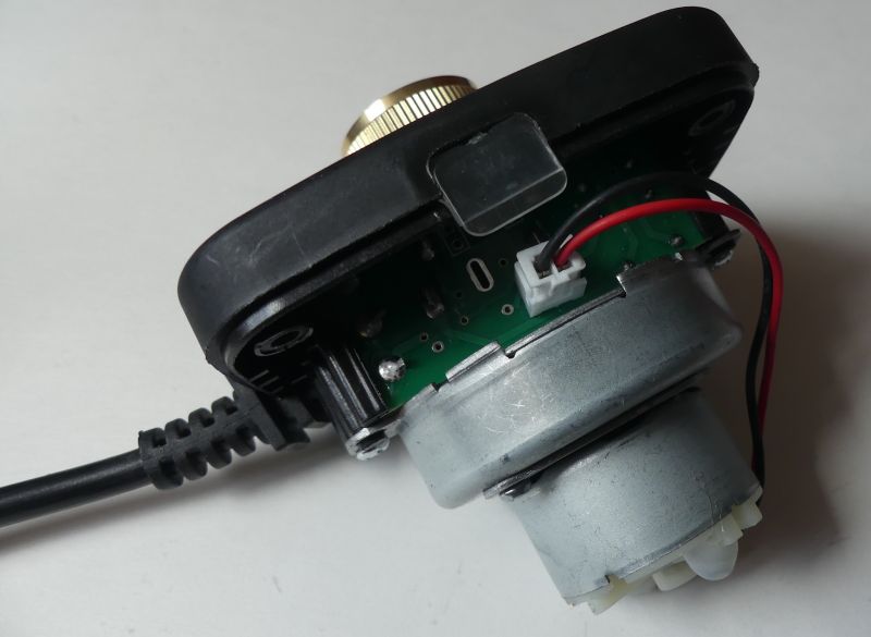 Inside an electronic device with a green PCB, red and black wires, and a metal DC motor attached