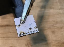 A clamp holding a small electronic board with several soldered connections.
