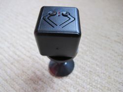 Cube-shaped mini spy camera on stand Mini spy camera in a black cube shape with two buttons and an LED on top, mounted on a stand.