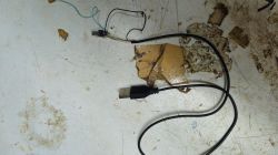 Black USB cable with exposed internal wires and a small connector on a dirty work surface