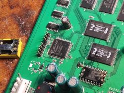Zbliżenie na płytę główną starego switcha z widocznymi układami scalonymi Intel TE28F128, kondensatorami i uszkodzonym elementem elektronicznym.
