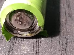 Damaged green cylindrical cell with visible leakage and corrosion on the positive terminal