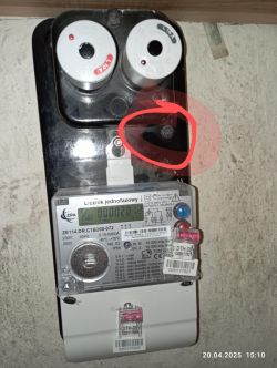 Zdjęcie licznika energii elektrycznej z czerwonym okręgiem wokół jednej ze śrub nad licznikiem.