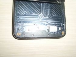 Zbliżenie na dolną część wnętrza wyświetlacza smartfona z widocznymi pinami i fragmentem metalowej blaszki.
