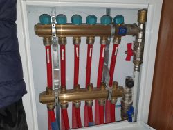 Zbliżenie na skrzynkę z instalacją ogrzewania podłogowego z czerwonymi rurami oraz zaworami w miedzianych przewodach.
