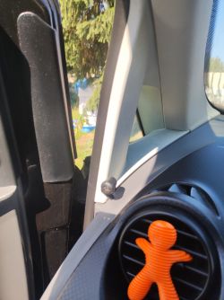 Wnętrze samochodu z widokiem na uchyloną szybę i pomarańczową ozdobę na kratce wentylacyjnej.