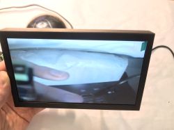 LCD screen showing camera feed, held in left hand, dome camera visible in background