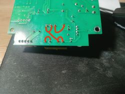 Spód zielonej płytki PCB z lutami i ścieżkami, z czerwonymi zaznaczeniami przy kilku punktach.