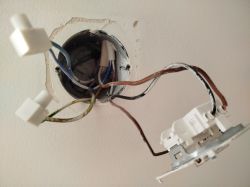 Widok wnętrza puszki elektrycznej z wystającymi kablami i przymocowanym przełącznikiem.