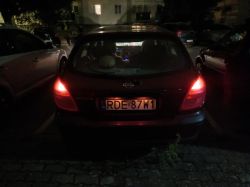 Tył czarnego samochodu Nissan na nocnym parkingu, widoczne czerwone tylne światła i tablica RDE 87W1