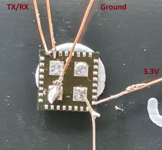 Close-up of a small electronic board with thin wires soldered and labeled TX/RX, Ground, and 3.3V.