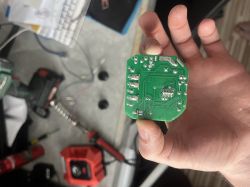 A person holds a green PCB with visible traces and soldering points in their hand.