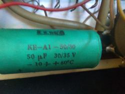 Zielony kondensator elektrolityczny z nadrukowanymi parametrami, otoczony przewodami.
