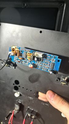 Niebieska płytka elektroniczna zamontowana na ciemnej obudowie z kablami i komponentami.