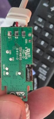 Small green printed circuit board with a white cable and electronic components, held between fingers.