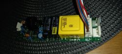 Widok płytki drukowanej z komponentami elektronicznymi, w tym przekaźnikami i kondensatorami.