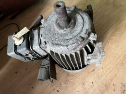 Stary silnik elektryczny z żebrowaniem chłodzącym i metalową obudową na tle drewnianej podłogi.