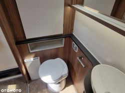 Interior of a camper van bathroom with a white toilet seat, sink, and wooden panels.