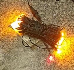 Zdjęcie zwiniętego łańcucha lampek LED, z większością światełek świecących na żółto, z jednym czerwonym światełkiem na dole.