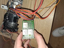 A person holding an electronic circuit with multiple wires and components on the floor.
