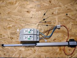 Two 12V power supplies, linear actuator, and rectifier diodes on wooden surface.