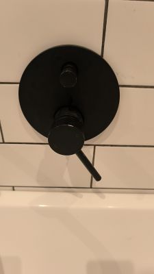 Czarny przełącznik w baterii podtynkowej zamontowany na białych kafelkach w łazience.