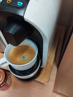 Ekspres Tchibo Cafissimo z filiżanką kawy, na blacie pod nim podkładka.
