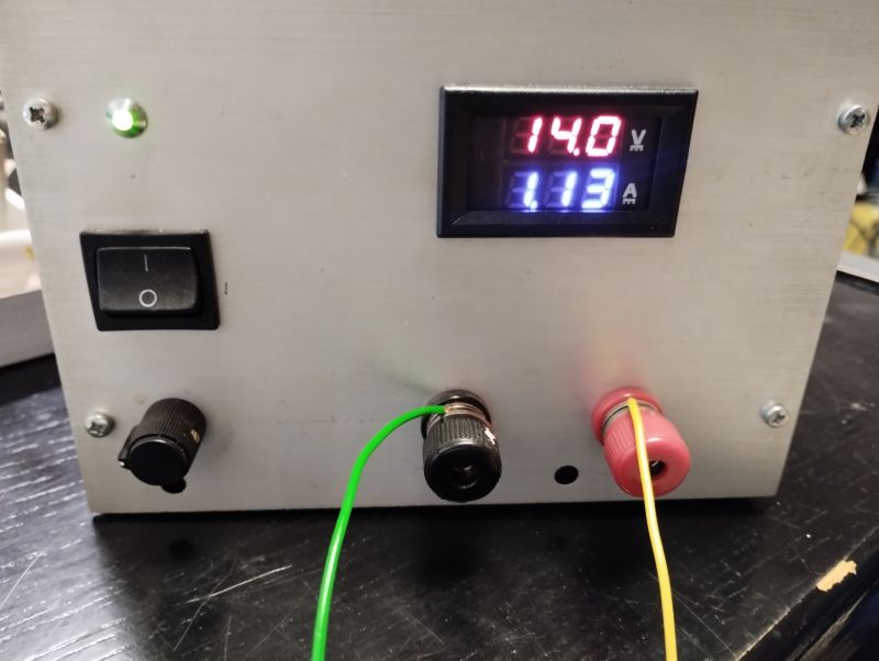 Panel zasilacza laboratoryjnego z wyświetlaczem napięcia 14,0V i prądu 1,13A, z podłączonymi przewodami.