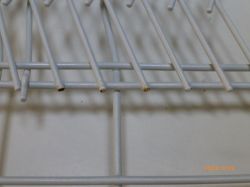 Zbliżenie na kosz zmywarki z widocznymi małymi plamami rdzy.