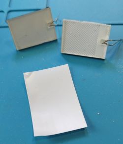 Two rectangular backlight panels with wires and a piece of paper on a blue surface.