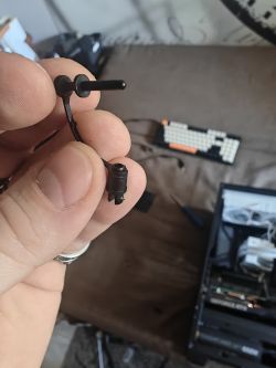 Ręka trzymająca plastikowy element na tle klawiatury i otwartej obudowy komputera.