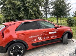 Czerwony SUV z okleiną „#GOelectric” i napisem „od 60 km zasięgu”, widok z boku na podjeździe
