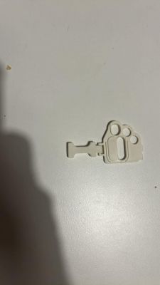 Plastikowy element z otworami i wypustkami, leżący na jasnej powierzchni.
