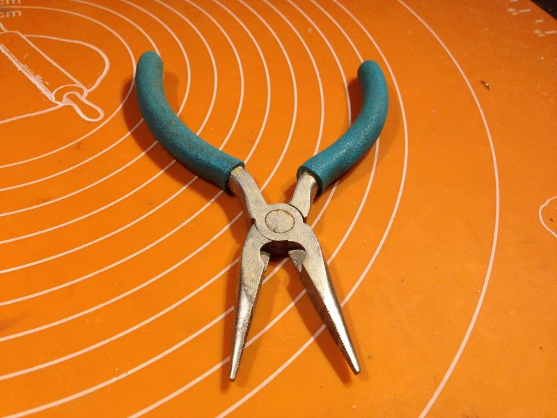 Długie szczypce do elektroniki z niebieskimi uchwytami na pomarańczowym tle.