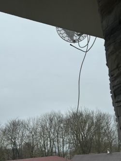 Antena satelitarna zamontowana nad balkonem z widocznymi drzewami w tle.
