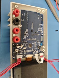 Wnętrze multimetru: płytka PCB z układami, złączami i czterema gniazdami bananowymi w obudowie