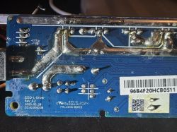 A circuit board with visible traces and soldered connections. A barcode label is visible at the bottom of the board.
