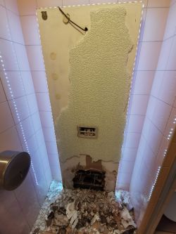 Zdemontowana ściana z widoczną strukturą spłuczki podwieszanej i rozsypanym gruzem na podłodze