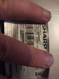 Sticker with serial number and model of Sharp LC-48CFE4042E TV visible under fingers.