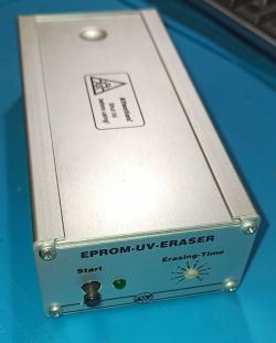 Srebrne urządzenie EPROM-UV-Eraser z przyciskami i pokrętłem na niebieskim tle.