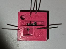 3D-printed chip holder with manually soldered wire connections Pink 3D-printed holder with a chip and thin soldered wires on sides