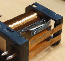 Zbliżenie na cewkę elektromagnetyczną w plastikowej obudowie z metalowymi przyłączami.