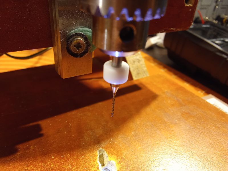 CNC milling machine with a drill bit above a wooden surface.
